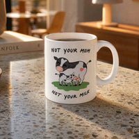 Mug with Bo the cow illustration and text "Not your cow, not your milk" on a countertop 