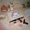 Makeup bag with a cartoon chicken design on a bathroom counter, alongside various makeup items.