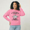Person wearing a pink sweatshirt with a cake character and the text "All you need is Love and vegan cake" on a white background 