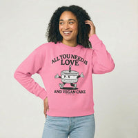 Person wearing a pink sweatshirt with a cake character and the text "All you need is Love and vegan cake" on a white background 