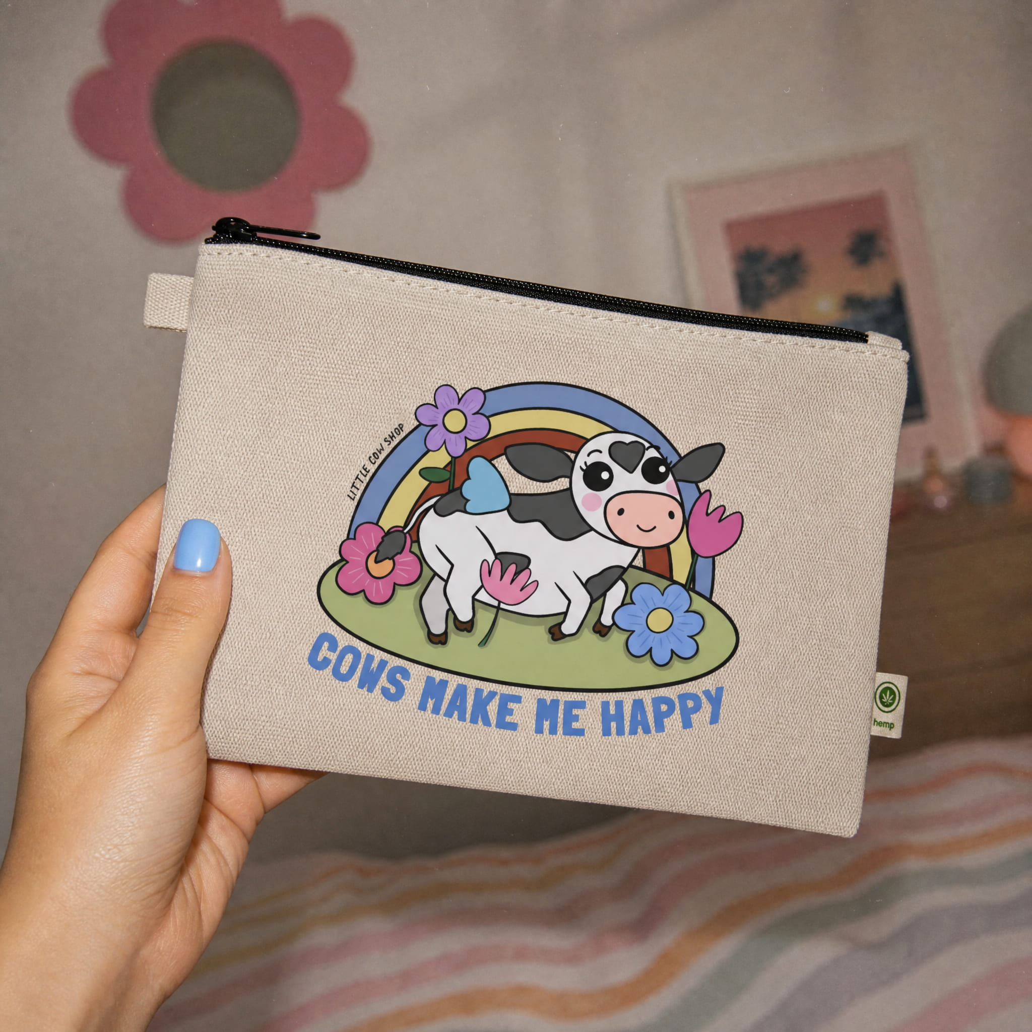 Beige pouch with cow illustration and 'Cows Make Me Happy' text held by a hand.
