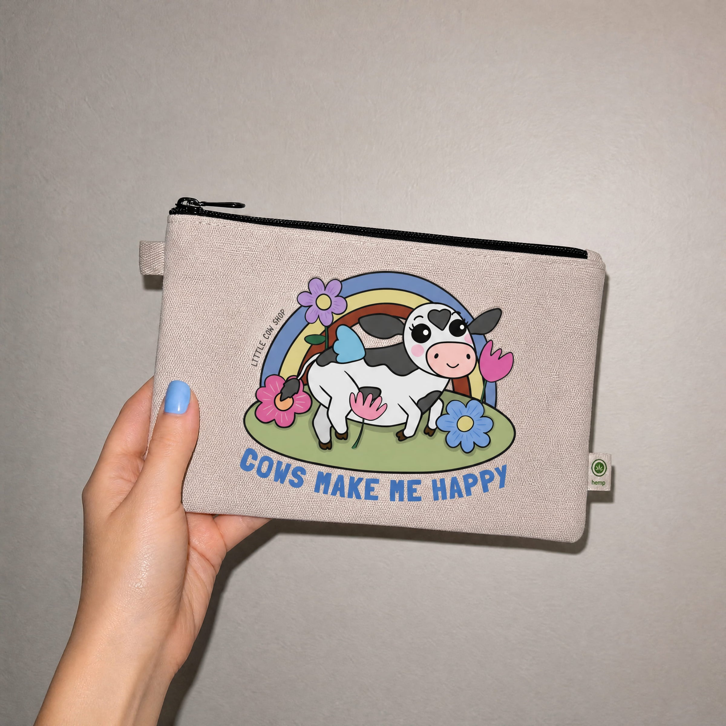 Beige pouch with a cow illustration and 'Cows Make Me Happy' text held by a hand against a plain background