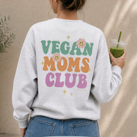 Person wearing a gray sweatshirt with 'Vegan Moms Club' text, holding a green smoothie.
