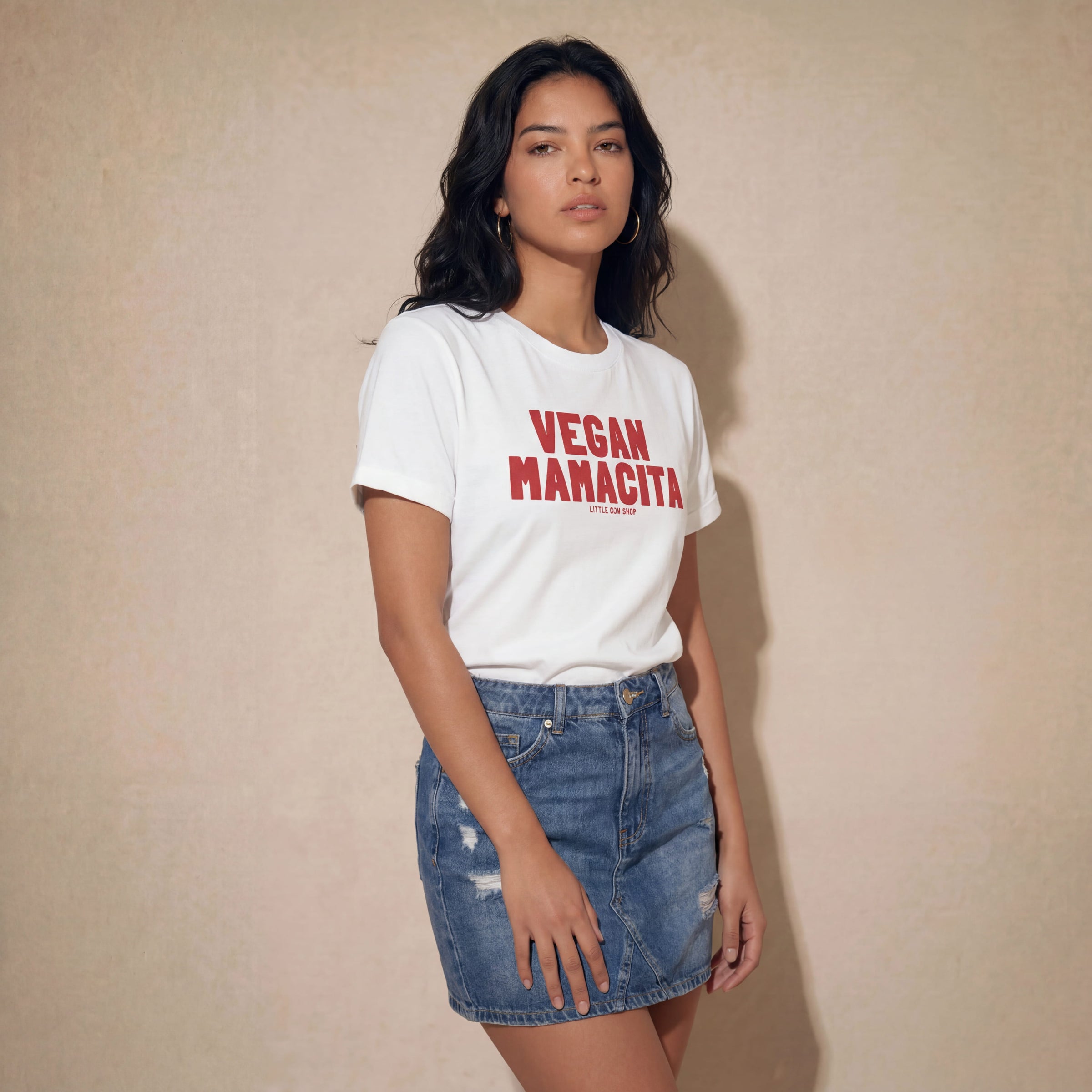 Woman wearing a white t-shirt with 'VEGAN MANACITA' red text and a denim skirt against a beige background