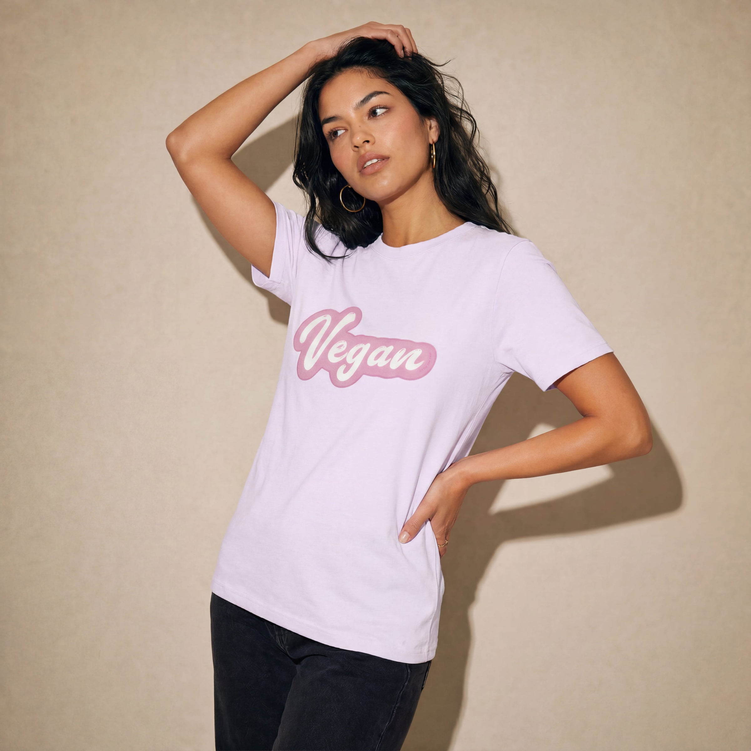 Woman wearing a white t-shirt with 'Vegan' in pink text against a beige background